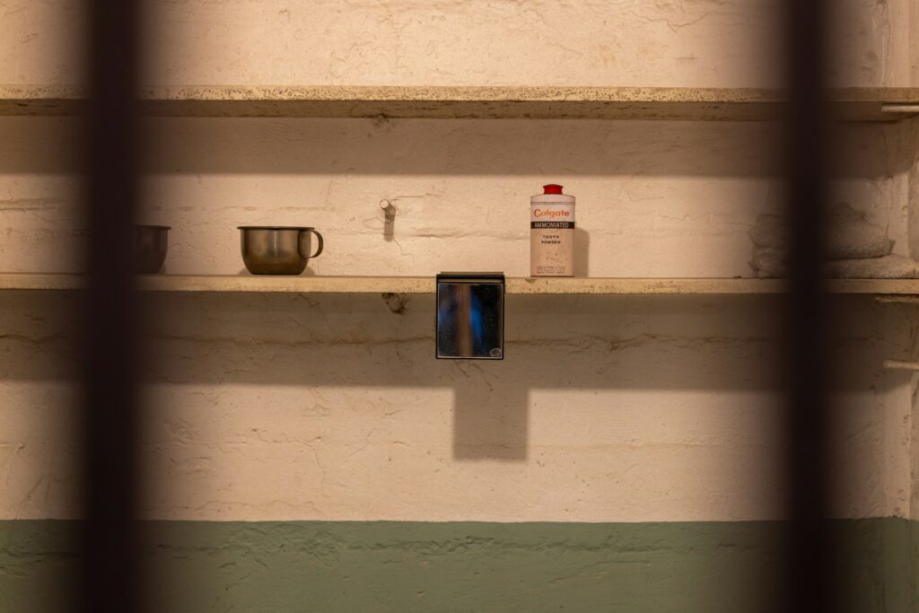 A cup and personal items on a cell shelf seen through prison bars
