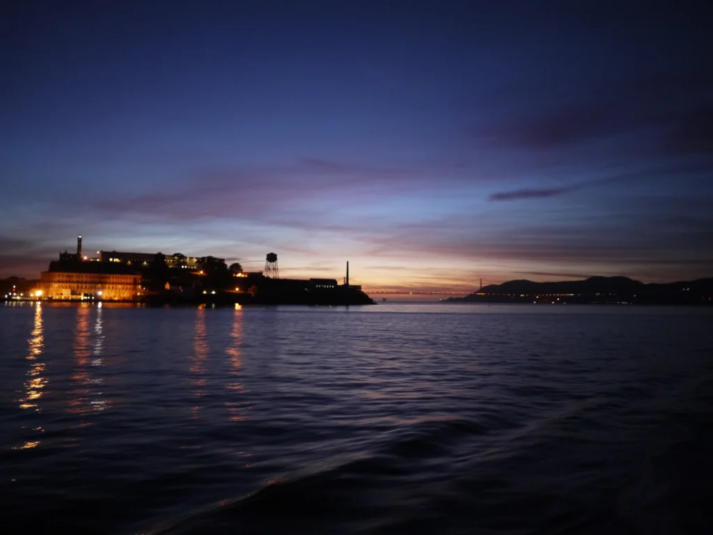 Alcatraz Island at dusk, its buildings lit up and reflected in San Francisco Bay
