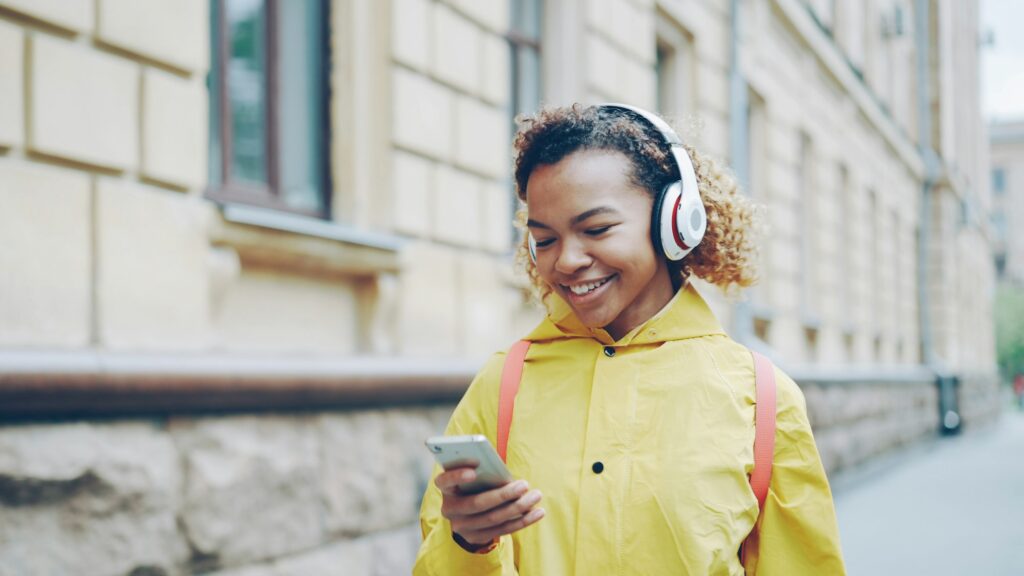 A smiling traveler with headphones looking at her phone